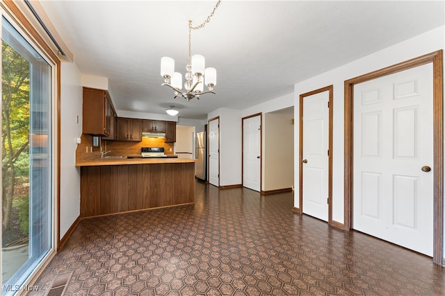 kitchen featuring kitchen peninsula, hanging light fixtures, stainless steel fridge, sink, and a notable chandelier