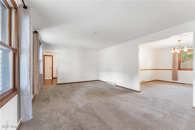 carpeted empty room with an inviting chandelier