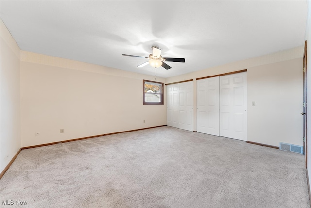 unfurnished bedroom with multiple closets, light carpet, and ceiling fan