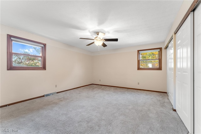 empty room with a wealth of natural light, light carpet, and ceiling fan