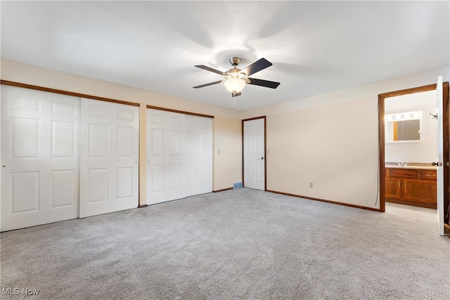 unfurnished bedroom with ceiling fan, light carpet, two closets, and ensuite bath