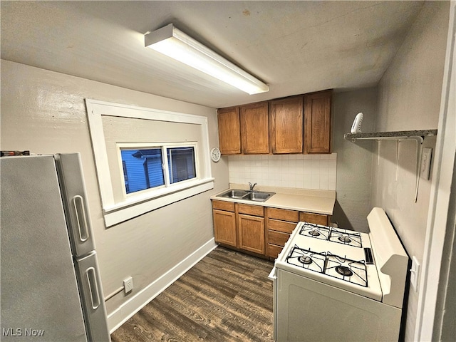 kitchen featuring dark wood-type flooring, backsplash, sink, white stove, and stainless steel refrigerator