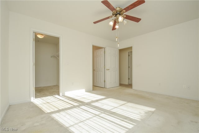 unfurnished bedroom featuring light carpet, a walk in closet, a closet, and ceiling fan