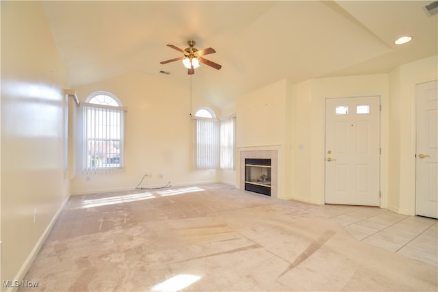 unfurnished living room featuring a tiled fireplace, vaulted ceiling, light colored carpet, and ceiling fan