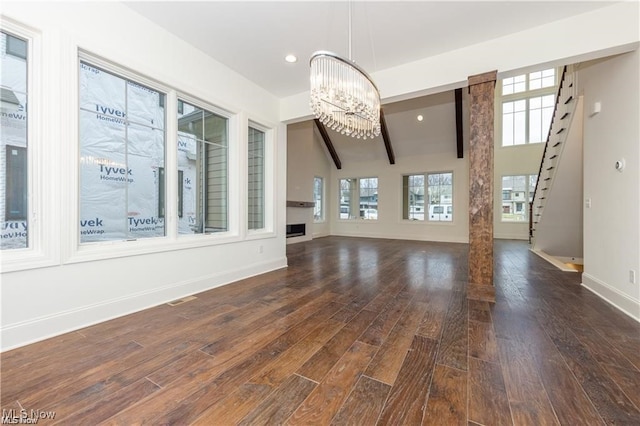 unfurnished living room with dark wood-type flooring, lofted ceiling with beams, and a chandelier