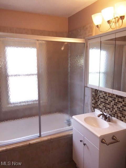 bathroom featuring vanity, combined bath / shower with glass door, and backsplash