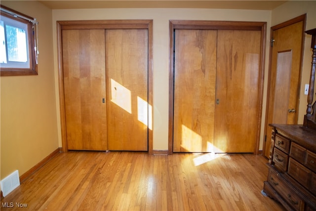 unfurnished bedroom with light wood-type flooring and two closets