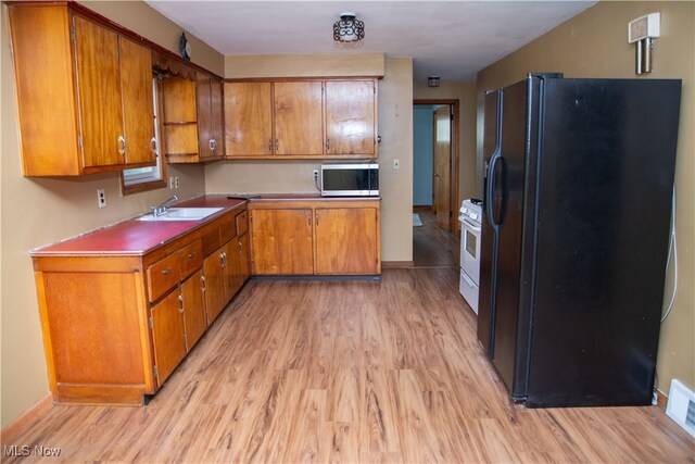 kitchen with white range with gas stovetop, light wood-type flooring, black fridge, and sink