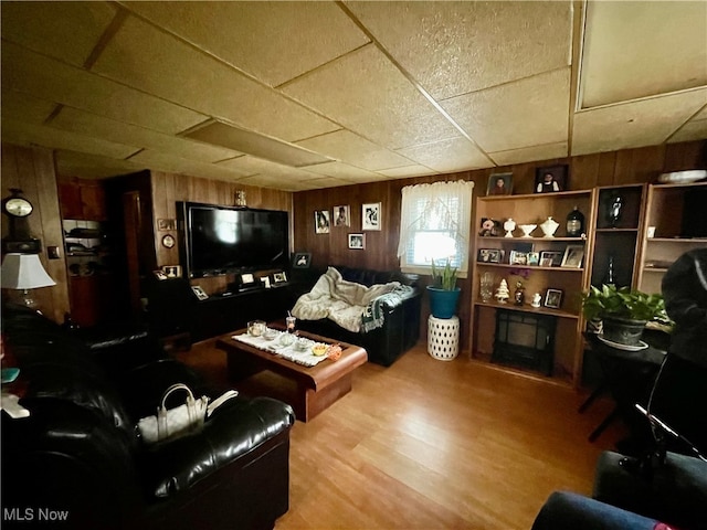 living room featuring wooden walls, hardwood / wood-style flooring, and a paneled ceiling