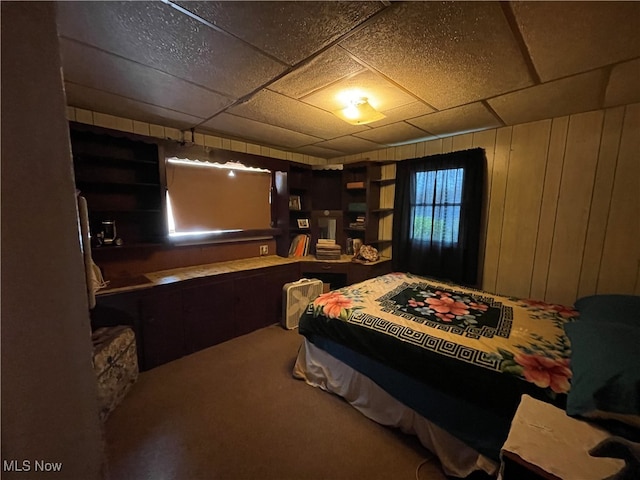 carpeted bedroom featuring a drop ceiling and wood walls