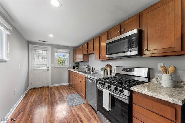 kitchen with appliances with stainless steel finishes, dark hardwood / wood-style floors, light stone counters, and sink