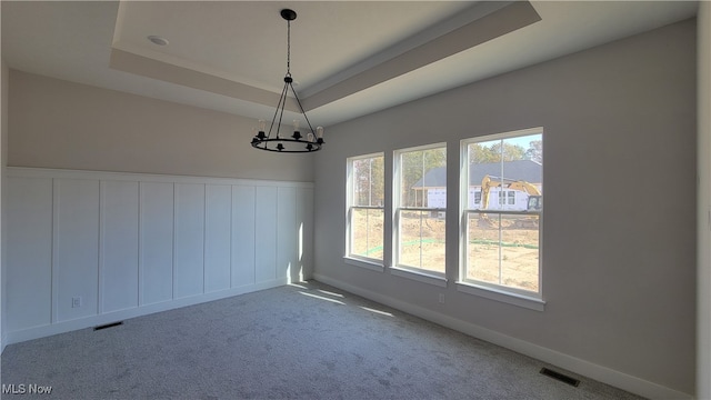 unfurnished dining area featuring a chandelier, a tray ceiling, and carpet flooring