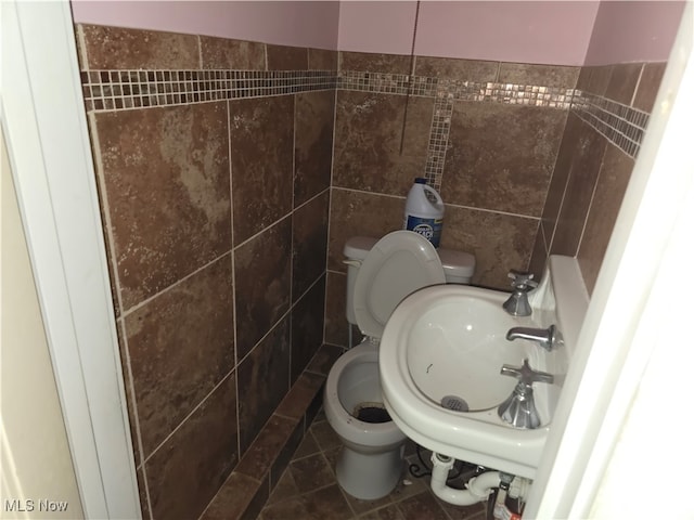 bathroom with toilet, tile patterned floors, and tile walls