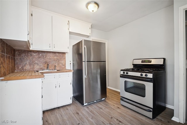 kitchen featuring gas range, white cabinets, light hardwood / wood-style floors, and stainless steel refrigerator