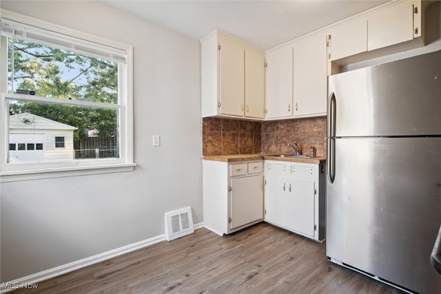 kitchen featuring stainless steel fridge, tasteful backsplash, white cabinetry, light wood-type flooring, and sink