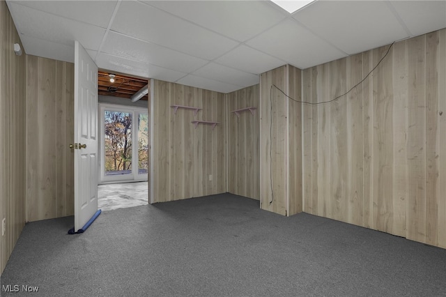 carpeted spare room with wood walls and a paneled ceiling