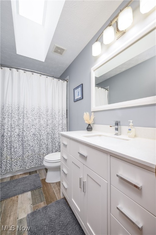 bathroom with wood-type flooring, a skylight, toilet, walk in shower, and vanity