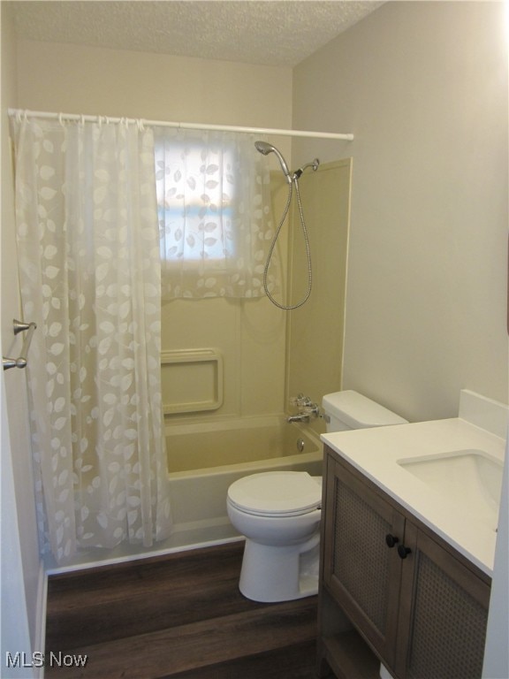 full bathroom with wood-type flooring, toilet, a textured ceiling, vanity, and shower / tub combo with curtain