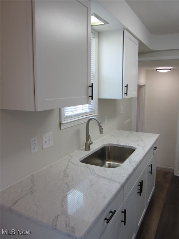 kitchen featuring white cabinets, light stone countertops, sink, and dark wood-type flooring