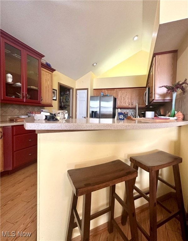 kitchen with kitchen peninsula, lofted ceiling, a breakfast bar, light wood-type flooring, and stainless steel refrigerator with ice dispenser