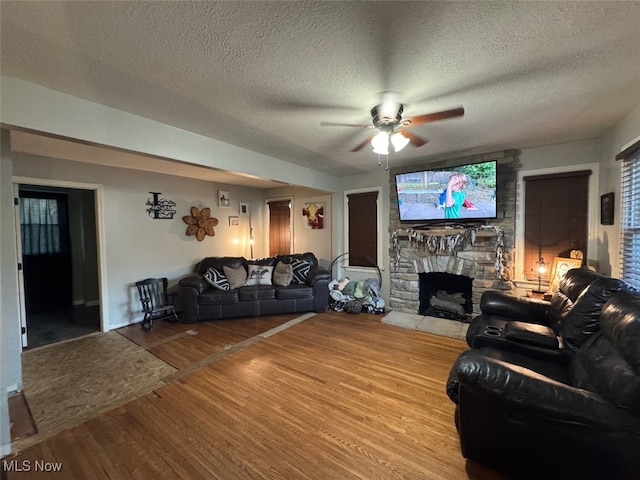 living room featuring hardwood / wood-style floors, a stone fireplace, a textured ceiling, and ceiling fan