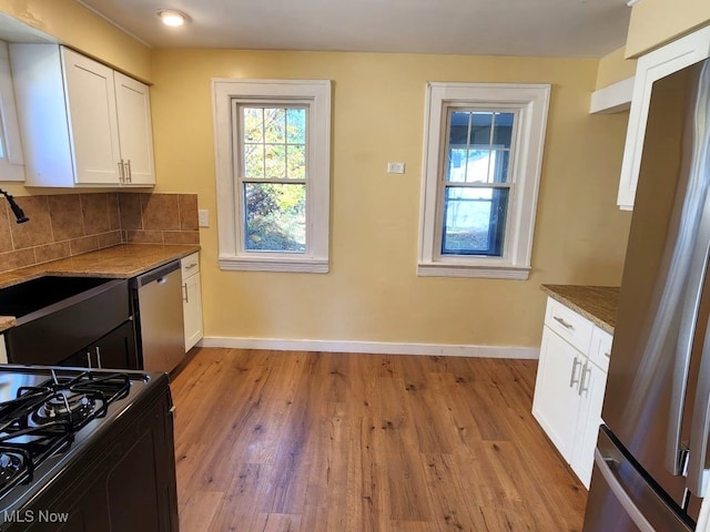 kitchen with stainless steel appliances, white cabinetry, dark stone counters, light hardwood / wood-style flooring, and decorative backsplash