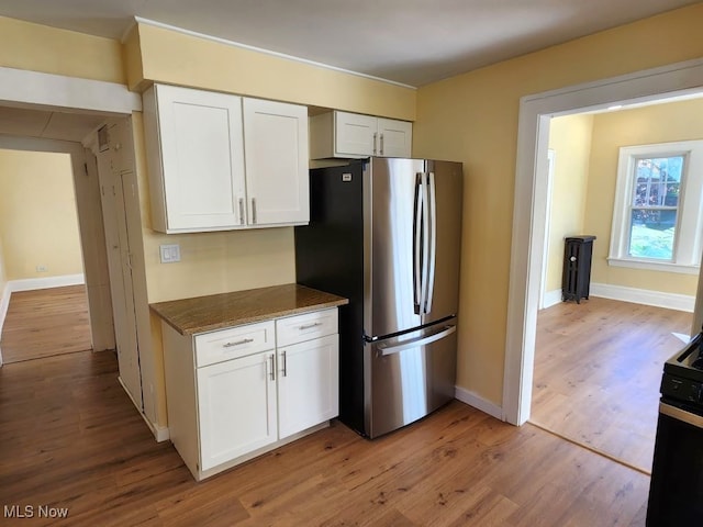 kitchen with white cabinets, stainless steel fridge, black range with electric stovetop, and light wood-type flooring