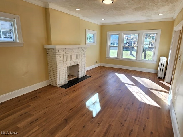 unfurnished living room with hardwood / wood-style flooring, radiator, a textured ceiling, crown molding, and a brick fireplace