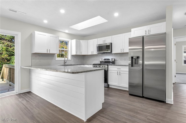 kitchen featuring stainless steel appliances, kitchen peninsula, stone countertops, and white cabinets