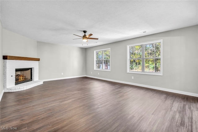 unfurnished living room featuring ceiling fan, a fireplace, dark hardwood / wood-style flooring, and a textured ceiling