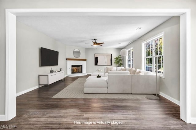 living room with a brick fireplace, dark wood-type flooring, and ceiling fan