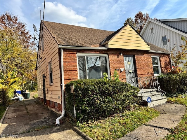 view of front of home featuring brick siding and roof with shingles