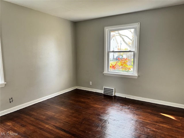 empty room featuring visible vents, baseboards, and dark wood-style floors