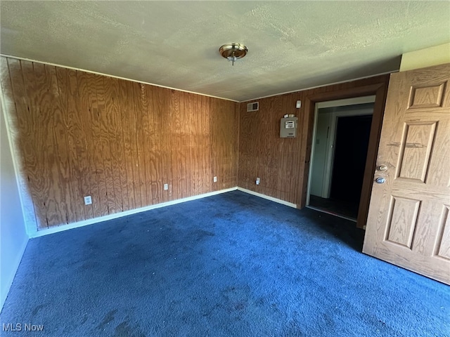 carpeted empty room featuring wooden walls and a textured ceiling