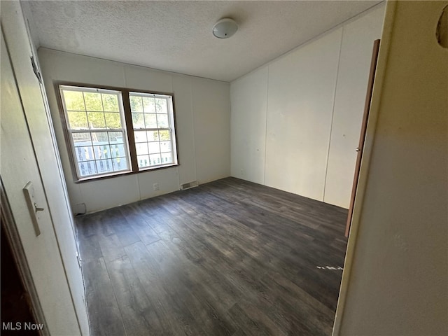 empty room with a textured ceiling and dark hardwood / wood-style flooring