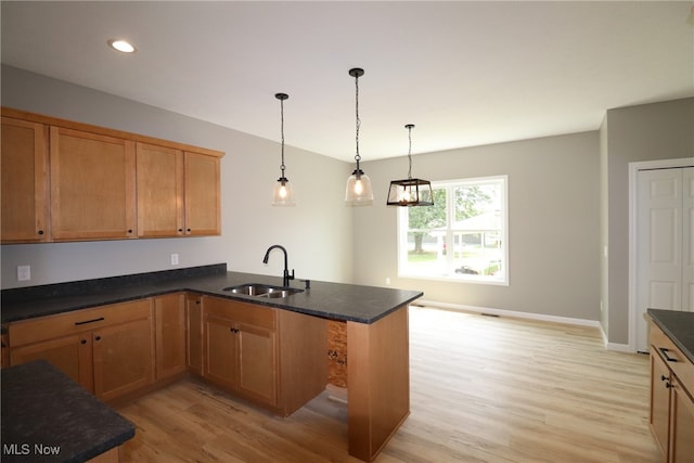 kitchen with kitchen peninsula, sink, light wood-type flooring, and pendant lighting