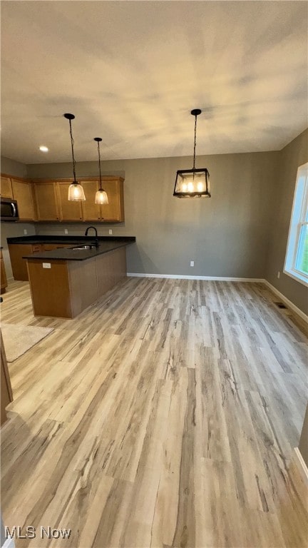 kitchen featuring sink, kitchen peninsula, pendant lighting, and light wood-type flooring