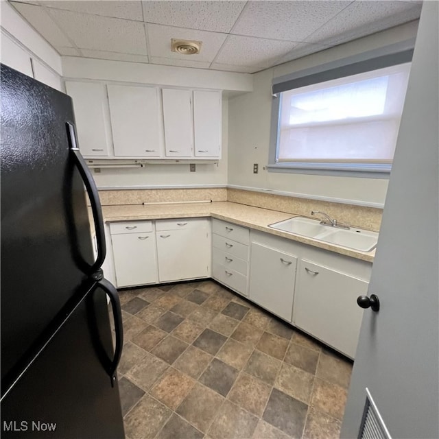 kitchen featuring white cabinetry, a drop ceiling, sink, and black refrigerator