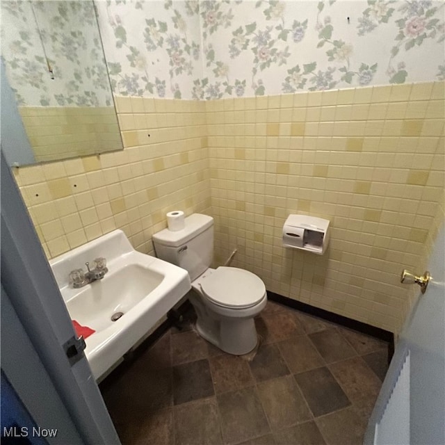 bathroom featuring toilet, sink, and tile walls