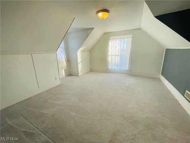 additional living space featuring vaulted ceiling and carpet flooring