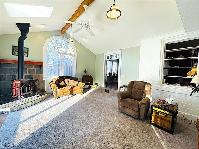 living room with ceiling fan, vaulted ceiling with skylight, carpet flooring, built in features, and a wood stove