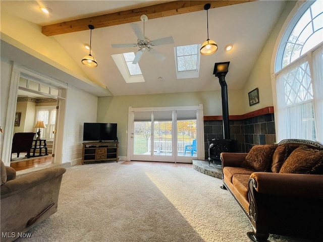 living room with ceiling fan, carpet floors, beamed ceiling, a skylight, and a wood stove