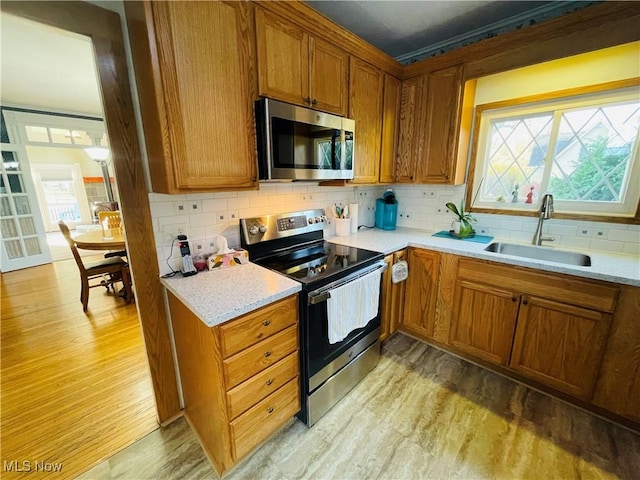 kitchen with backsplash, appliances with stainless steel finishes, sink, and light hardwood / wood-style flooring