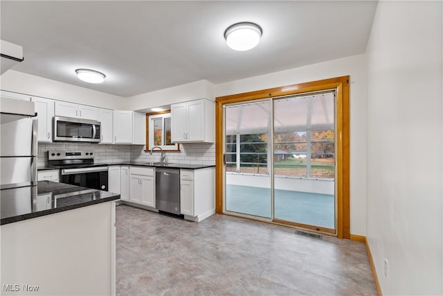 kitchen featuring white cabinetry, backsplash, stainless steel appliances, and dark stone counters