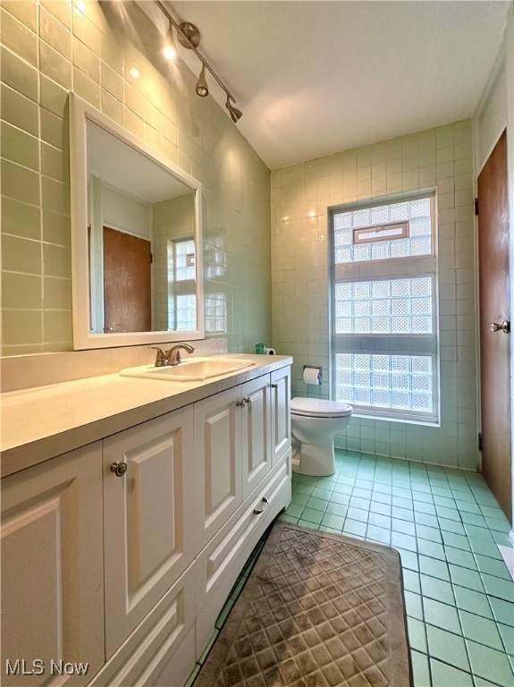 bathroom with toilet, vanity, tile walls, and tile patterned flooring