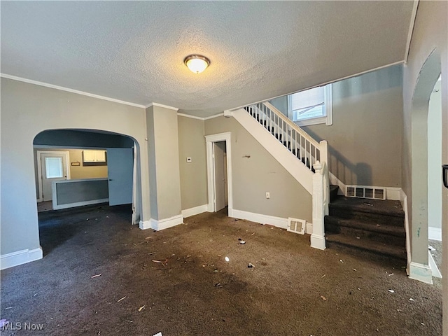 unfurnished living room with a textured ceiling, ornamental molding, and dark colored carpet