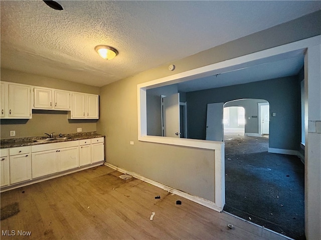 kitchen with a textured ceiling, wood-type flooring, sink, and white cabinets