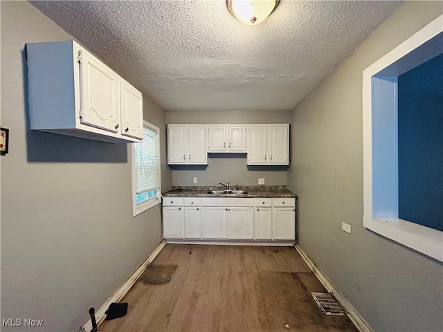 kitchen with sink, white cabinets, a textured ceiling, and light wood-type flooring