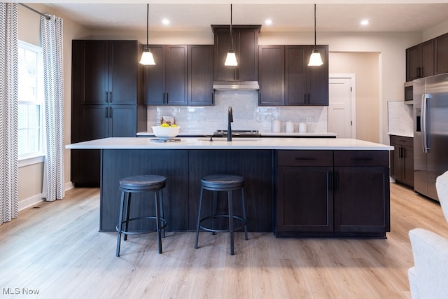 kitchen with stainless steel refrigerator with ice dispenser, a center island with sink, light wood-type flooring, and pendant lighting