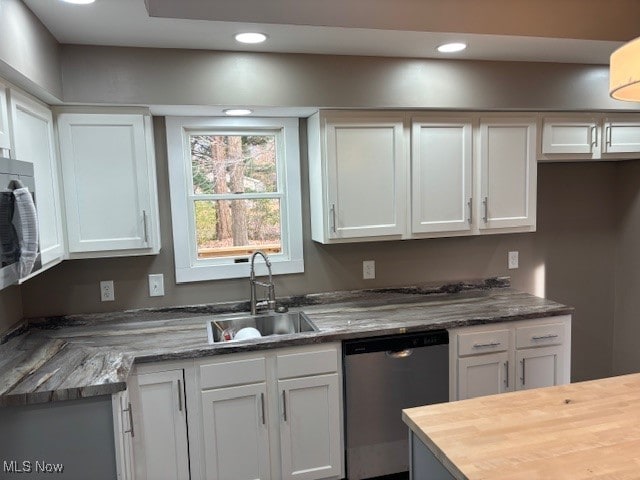 kitchen with stainless steel dishwasher, sink, white cabinets, and dark stone countertops